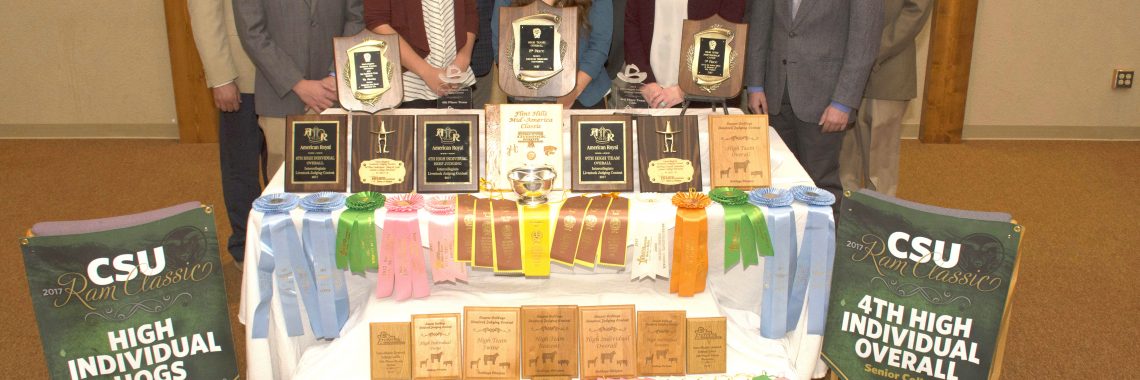 11 people standing behind table full of awards and ribbons.