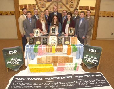 11 people standing behind table full of awards and ribbons.