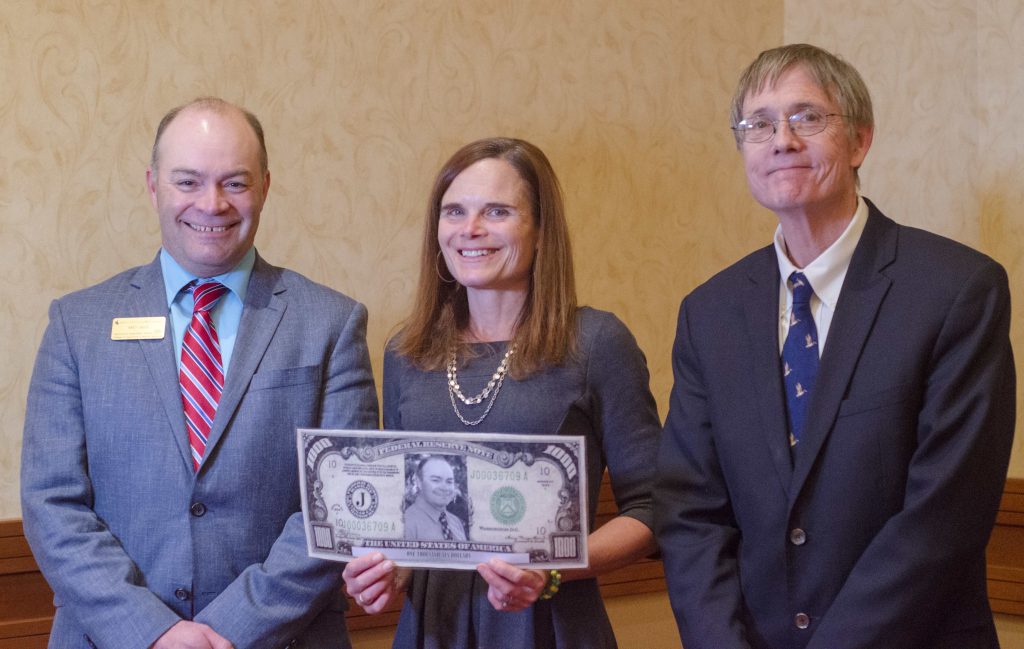 Award winner holding pretend money and flanked by two men.