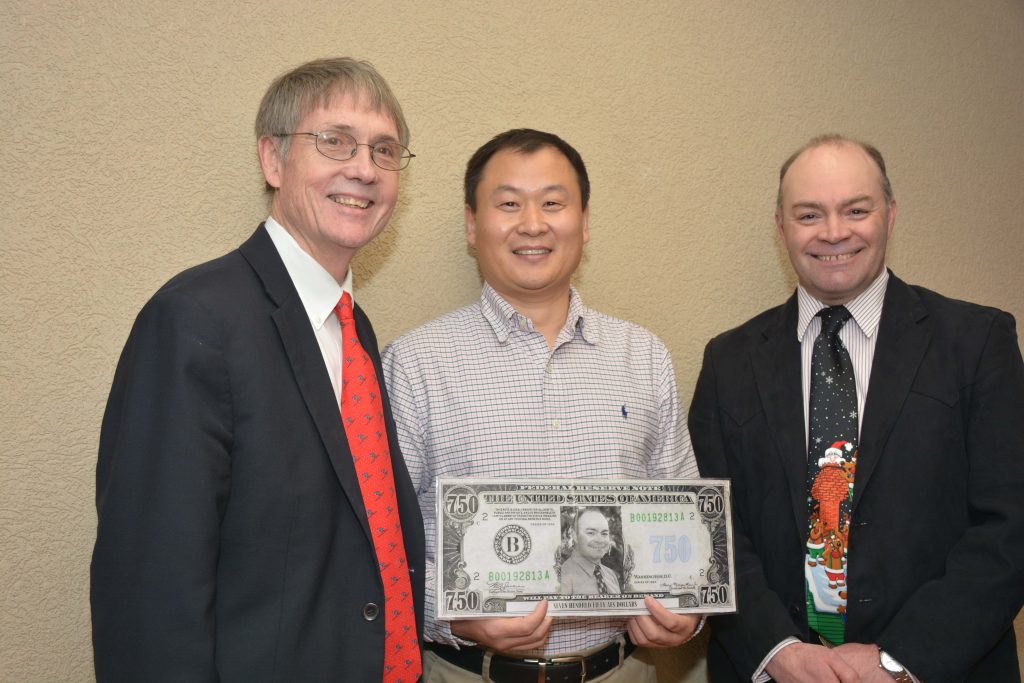 Award winner holding pretend money and flanked by two men.