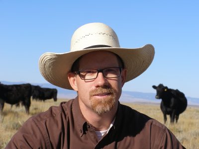 Man wearing hat in pasture with cows behind him