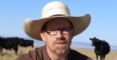 Man wearing hat in pasture with cows behind him