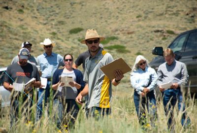 Man in hat points out plants to  group of people in field.