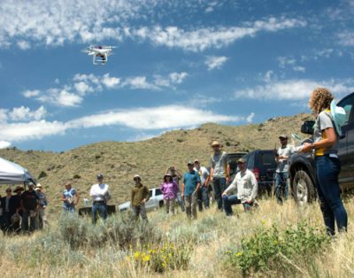 Woman flying a drone while group of people observers.