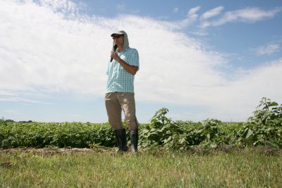 Man in hat standing in a field with microphone