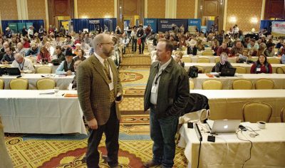 Photograph of two men standing in front of conference attendees