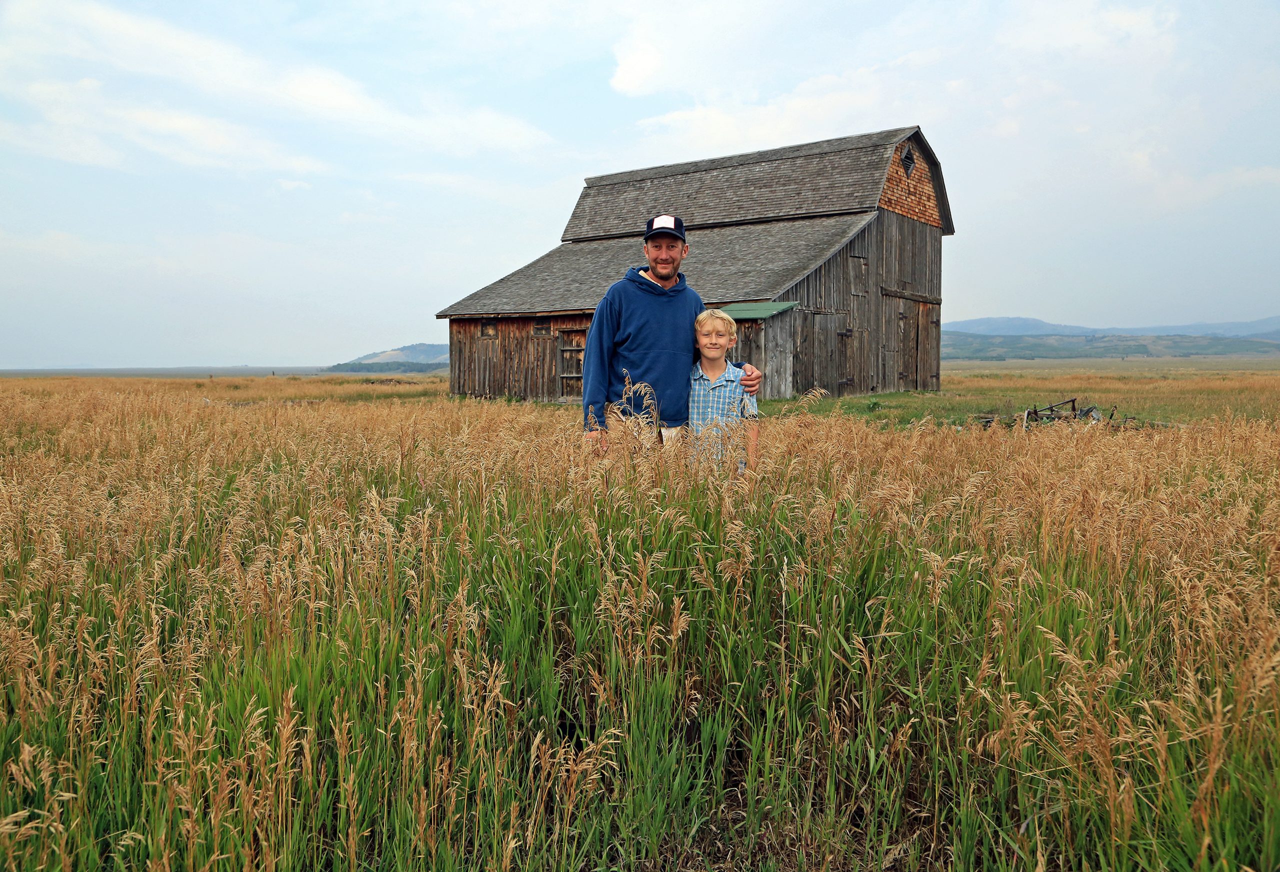 Father and son in field in front of old brown barn.