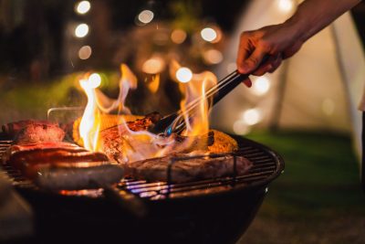 various meats on grill with flames and someone reaching in with tongs to flip one of the pieces of meat