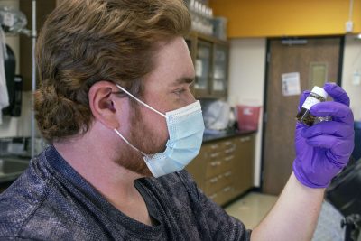 Photograph of student holding a vial of insects suspended in a liquid