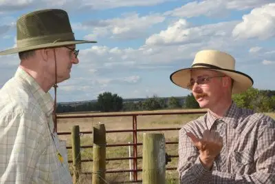 Photograph of two men talking by a fence