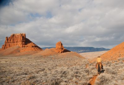 Riding a horse on the range near Shell, Wyoming. Red rock formations in the background.