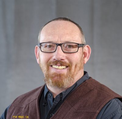 portrait of smiling man with red beard wearing glasses and vest