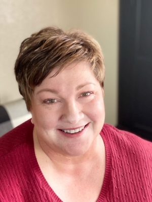 Woman in red shirt seated at her desk.