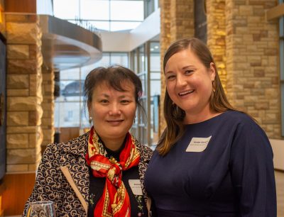 smiling woman wearing red scarf stands beside smiling woman in blue shirt