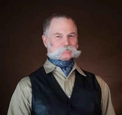Headshot of man with mustache wearing tan shirt and black vest