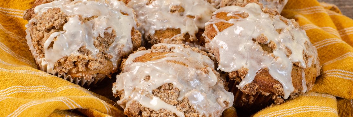 5 streusel topped muffins with vanilla icing drizzle in a yellow towel