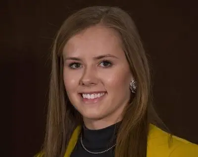 headshot of smiling woman wearing black shirt and yellow jacket