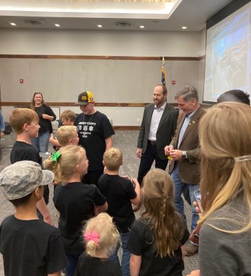 group of children wearing black t-shirts chat with the governor of Wyoming while several smiling adults look on