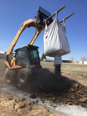 skid steer empties bag of coal char onto pile of manure