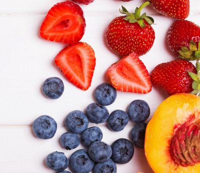 strawberries, blueberries, and a sliced peach scattered on a white background