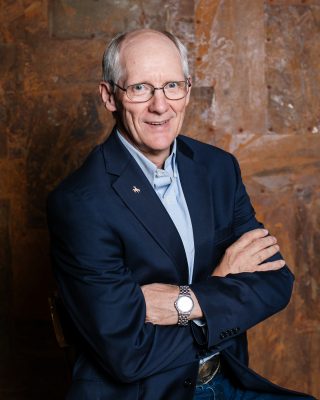 smiling man with grey hair and glasses wearing blue blazer