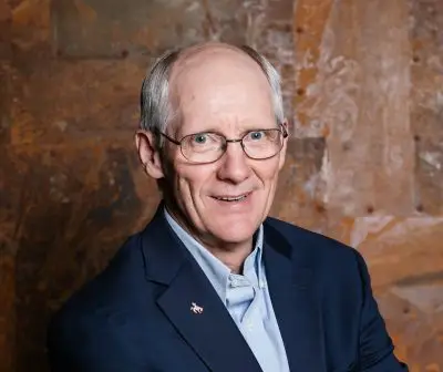 smiling man wearing glasses and navy blue blazer