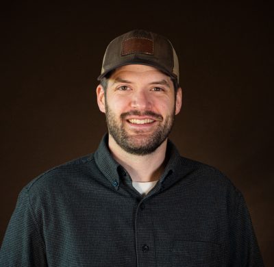 smiling bearded man with baseball cap and black button-down shirt