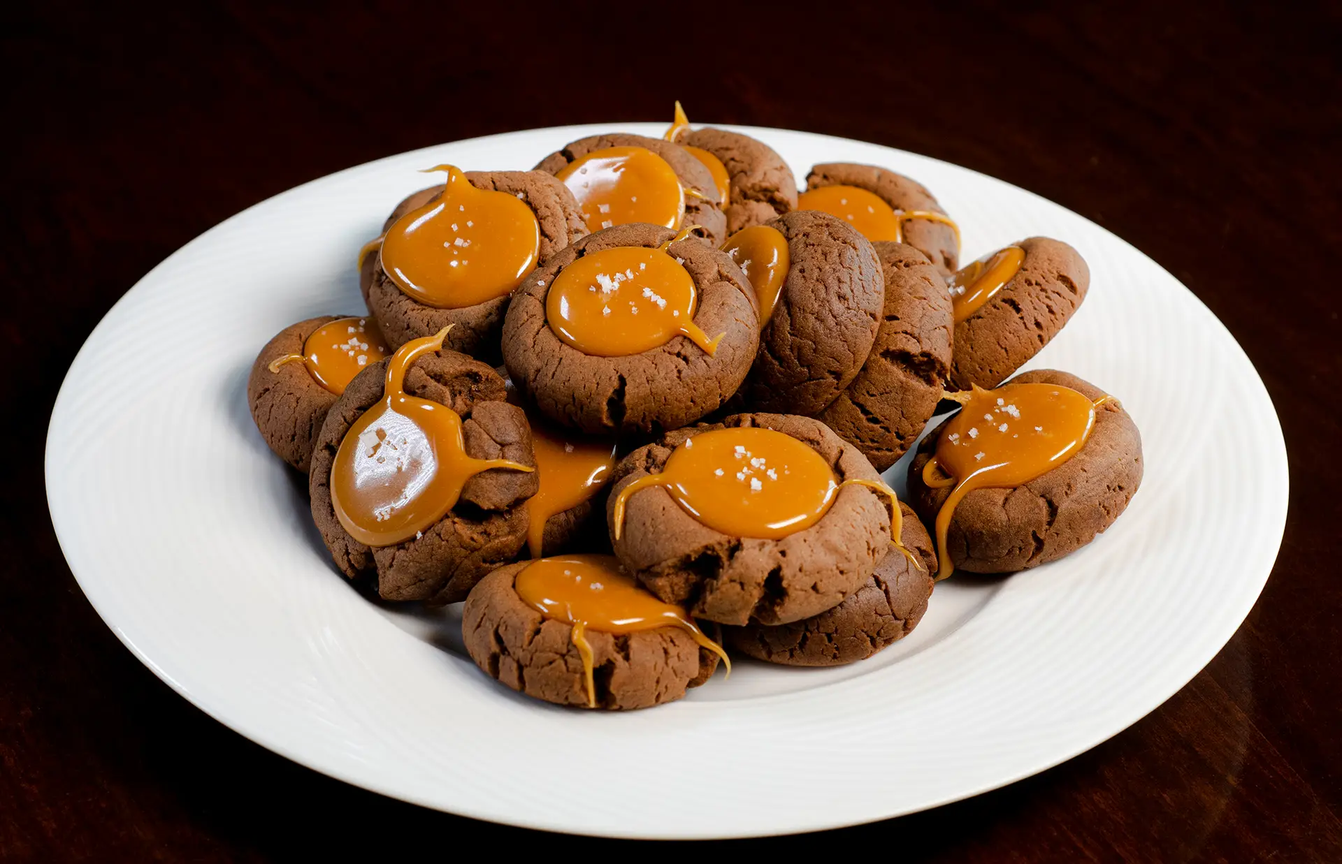 plate of chocolate thumbprint cookies with caramel centers sprinkled with a few grains of salt