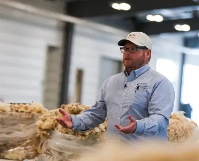 man wearing UW baseball cap and shirt presents in front of bags of wool