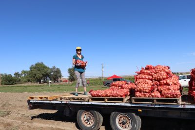 smiling woman stands on flatbed trailer holding a bag of potatoes