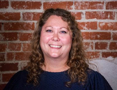 smiling woman with curly hair and blue eyes and blue shirt