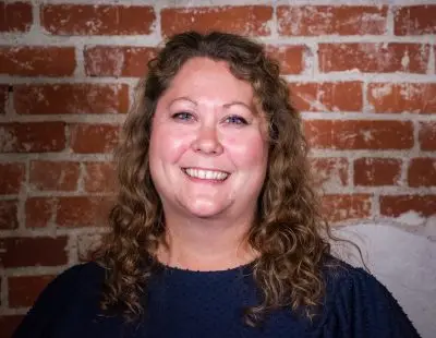 smiling woman with curly hair and blue eyes and blue shirt