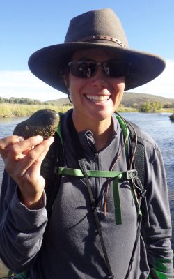 smiling woman wearing hat and sunglasses holds up a freshwater mussel