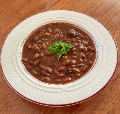 white dish with red rim filled with baked beans and sprig of green herb as garnish