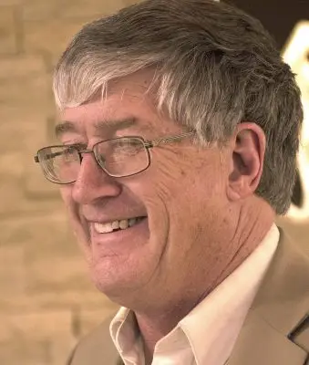 smiling man with grey hair wearing glasses and tan coat
