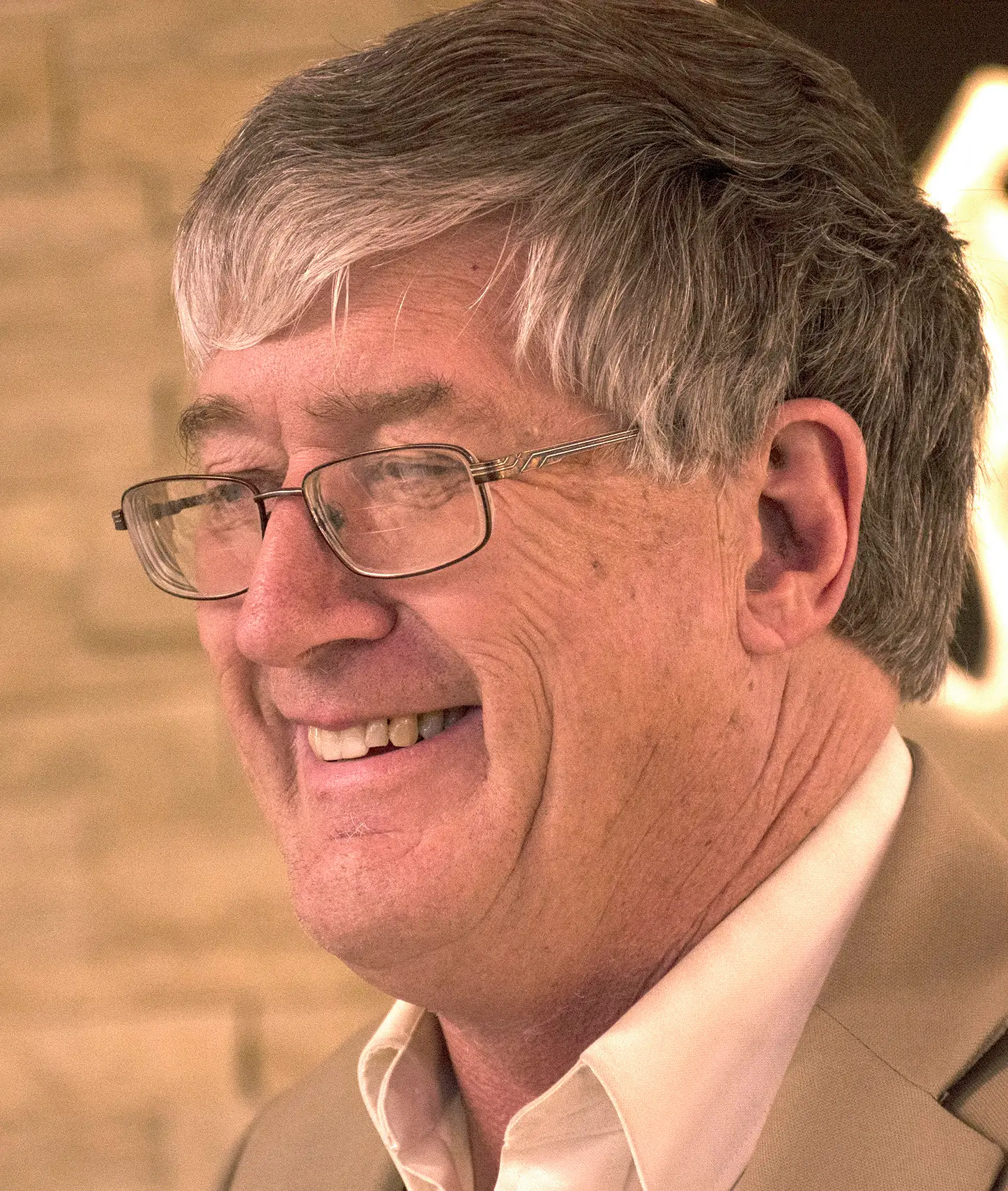 smiling man with grey hair wearing glasses and tan coat