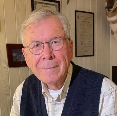 portrait of smiling man with grey hair wearing glasses and blue vest