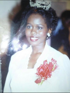 portrait of smiling pageant winner wearing a tiara and red corsage pinned to a white dress