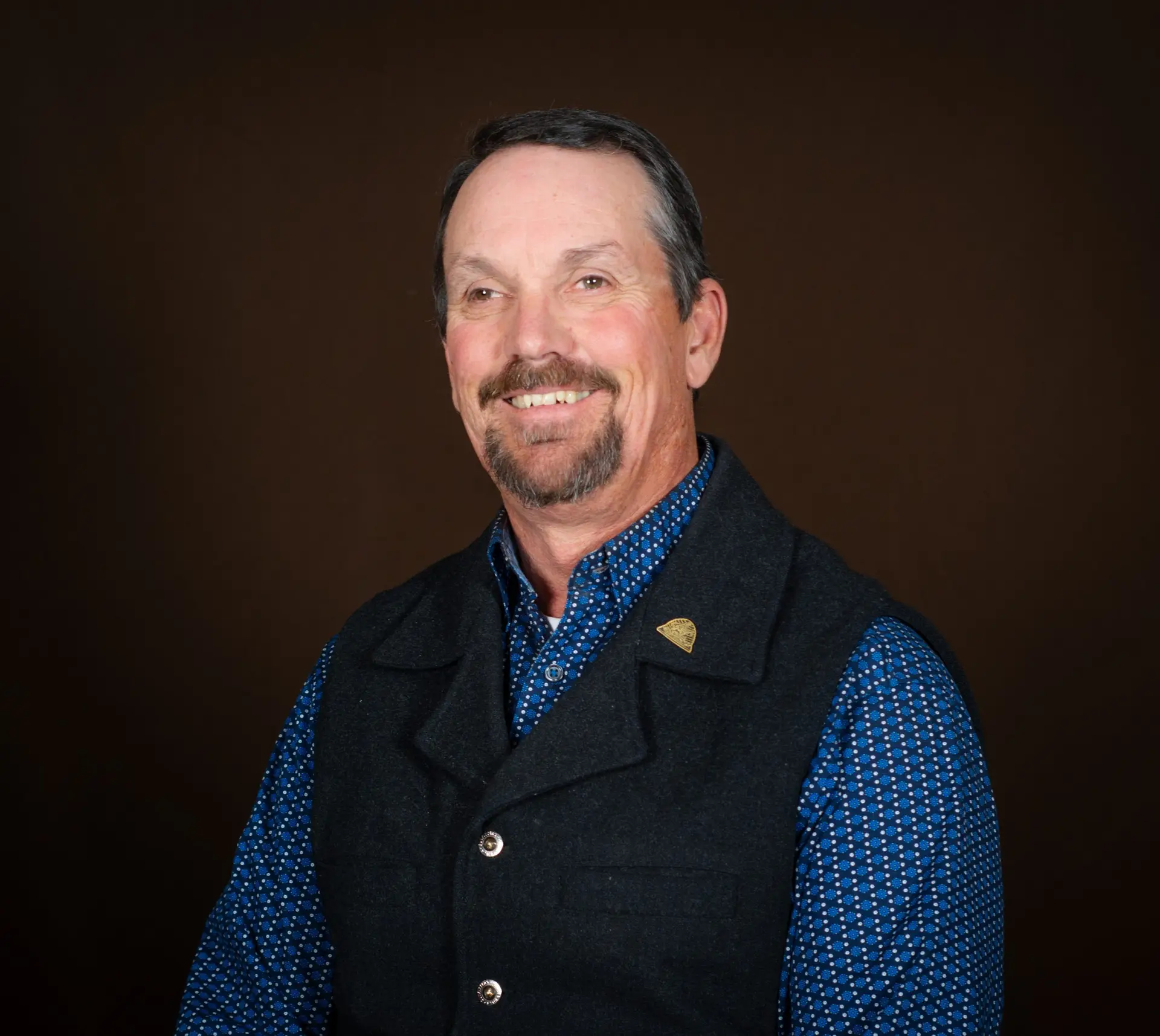 portrait of bearded man wearing blue patterned shirt and dark gray vest