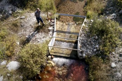 aerial view of man wearing waders standing beside a flume in an irrigation ditch