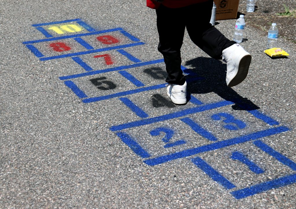 student wearing black pants and white shoes hops on newly painted hopscotch squares on gray pavement