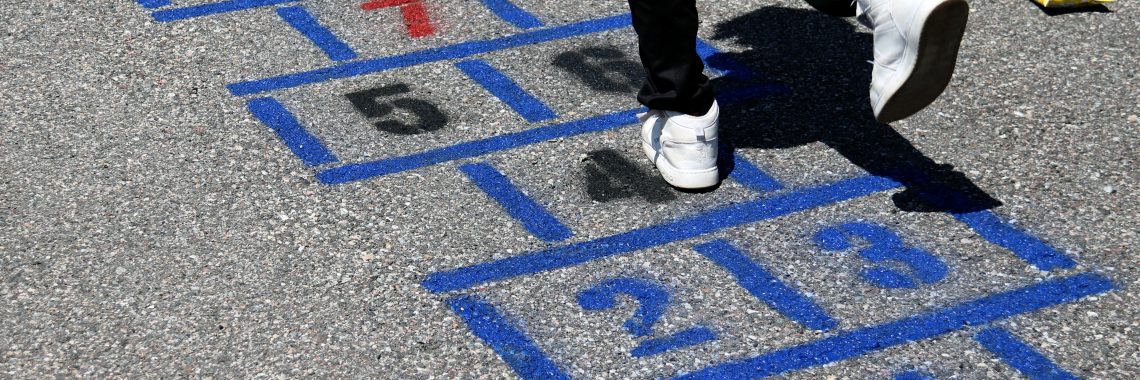 student wearing black pants and white shoes hops on newly painted hopscotch squares on gray pavement