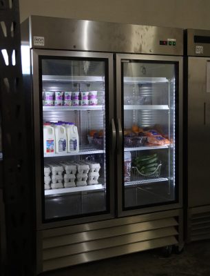 industrial fridge with glass front containing milk, eggs, produce, and yogurt.