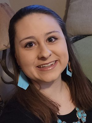 Smiling woman with dark hair wearing dangly turquoise earrings and matching necklace and a black shirt