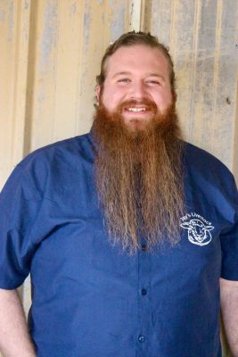 smiling man with long red beard wearing blue button down shirt with Jay's Livestock logo