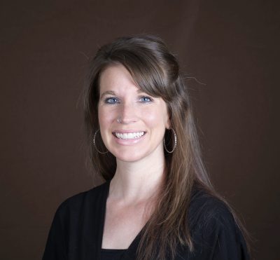 Headshot of smiling woman with brown hair and side bangs wearing large hoop earrings and black shirt