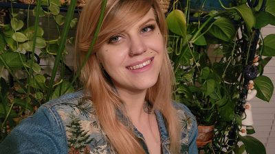 portrait photo of smiling blond woman wearing an embroidered jean jacket and surrounded by plants