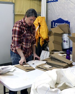 woman wearing flannel shirt and jeans stands over a white plastic table with flattened brown bags on top