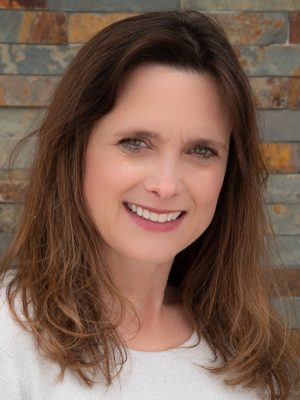 Close-up portrait of brown-haired woman wearing a white shirt with decorative tile in the background