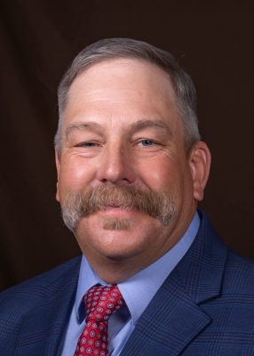 portrait of man with mustache wearing blue jacket over blue colored shirt and red tie